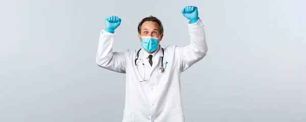 Covid-19, Prävention von Viren, Gesundheitspersonal und Impfkonzept. Glücklich aufgeregter Arzt in medizinischer Maske und Handschuhen hebt die Hände und schreit Ja, gewinnt, feiert Sieg oder Erfolg — Stockfoto