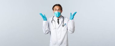 Covid-19, virüsü önleme, sağlık çalışanları ve aşı konsepti. Tıbbi maskeli ve eldivenli endişeli doktor, elleri tedirgin bir şekilde bakıyor, beyaz arka planda panik var.