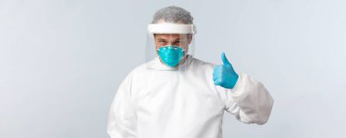 Covid-19, virüsü önleme, sağlık çalışanları ve aşı konsepti. Korunma ekipmanları içinde kendine güvenen bir doktor. Baş parmağını kaldır ve her şeyin yoluna gireceğinden emin ol.