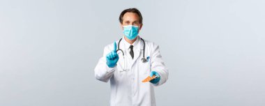 Covid-19, virüsü önleme, sağlık çalışanları ve aşı konsepti. Tıbbi maskeli doktor ve eldivenler reçeteyi açıklar, ilaç verir, bir parmağını gösterir ve hastaya ilaç verir.