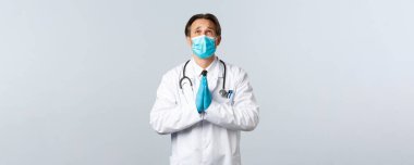 Covid-19, virüsü önleme, sağlık çalışanları ve aşı konsepti. Tıbbi maskeli ve eldivenli ümitsiz doktor Tanrı 'ya yalvarıyor, dua ediyor, yalvarıyor.