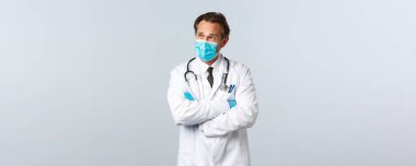 Covid-19, virüsü önleme, sağlık çalışanları ve aşı konsepti. Tıbbi maskeli ve eldivenli sorunlu doktor, sol üst köşeye bakıyor endişeli, kararını düşünüyor.