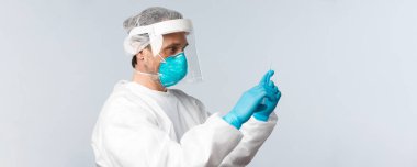 Covid-19, virüsü önleme, sağlık çalışanları ve aşı konsepti. Kişisel koruyucu ekipmanlarda doktorun profil fotoğrafı. Şırıngayı koronavirüs aşısıyla doldur, hasta hastayı tedavi et.