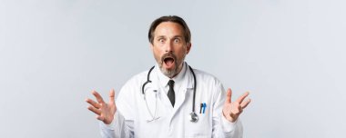 Covid-19, virüsü önleme, sağlık çalışanları ve aşı konsepti. Şok olmuş ve endişeli doktor beyaz önlüklü. Çenesi düşmüş, soluk soluğa kalmış. Kötü haberleri duyun, korkuyla el kaldırın.