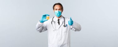 Covid-19, virüsü önleme, sağlık çalışanları ve aşı konsepti. Her şey yolunda. Tıbbi maskeli ve eldivenli doktor idrar örneğini inceler ve onaylı beyaz arka planda baş parmağını kaldırdığını gösterir.