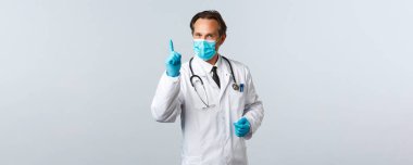 Covid-19, virüsü önleme, sağlık çalışanları ve aşı konsepti. Tıbbi maskeli profesyonel orta yaşlı doktor ve parmak gösteren eldivenler, Coronavirus sosyal mesafesi sırasında kuralları açıklar.