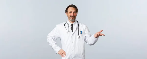 Covid-19, coronavirus outbreak, healthcare workers and pandemic concept. Skeptical and confused male doctor in white coat, pointing right with dismay or irony, grimacing disappointed — Stock Photo, Image