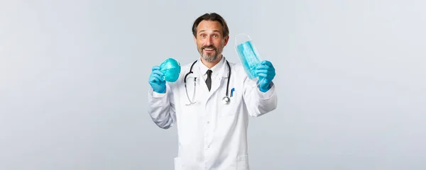 Covid-19, prevenção de vírus, profissionais de saúde e conceito de vacinação. Médico sorridente amigável prefere usar máscara médica em vez de respirador, de pé em luvas e casaco branco — Fotografia de Stock