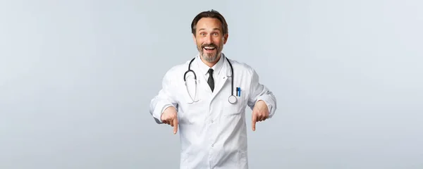 Covid-19, brote de coronavirus, trabajadores sanitarios y concepto pandémico. Feliz sonriente médico masculino en bata blanca invitando a hacer clic en el enlace. Terapeuta mostrando el camino a la publicidad, invitando a los pacientes — Foto de Stock