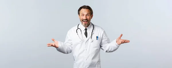 Covid-19, coronavirus outbreak, healthcare workers and pandemic concept. Surprised happy male doctor receive great news, congratulating patient for releasing hospital, white background — Stock Photo, Image