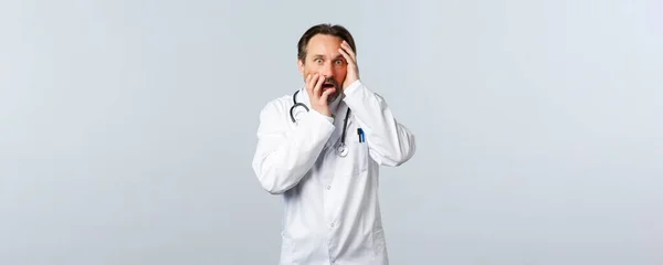 Covid-19, coronavirus outbreak, healthcare workers and pandemic concept. Shocked and worried male doctor in white coat, gasping, looking scared with panic at camera — Stock Photo, Image