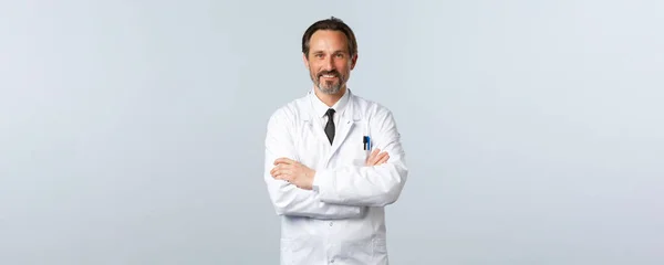 Covid-19 、コロナウイルスの発生、医療従事者およびパンデミックの概念。白衣クロス腕胸の中年の医師,患者を助ける準備ができて,薬を処方,陽気な笑顔 — ストック写真