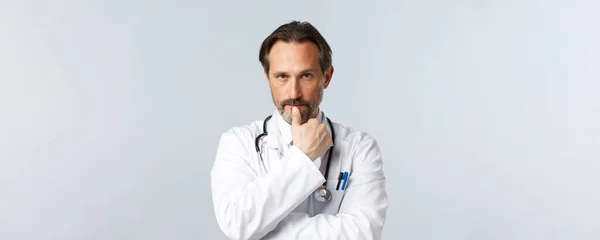 Covid-19, preventing virus, healthcare workers and vaccination concept. Close-up of concerned serious-looking doctor in white coat, biting finger and looking focused, listening to patient symptoms — Stock Photo, Image