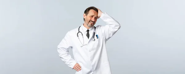 Covid-19, koronavirüs salgını, sağlık çalışanları ve pandemik konsept. Sıkıntılı ve endişeli beyaz önlüklü erkek doktor, dokunuyor ve yüzünü buruşturuyor. — Stok fotoğraf