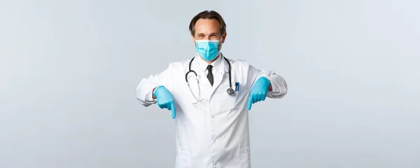 Covid-19, prevenzione di virus, operatori sanitari e concetto di vaccinazione. Piacevole medico in maschera medica e guanti dare consigli, raccomandare promo, puntando il dito verso il basso al banner — Foto Stock