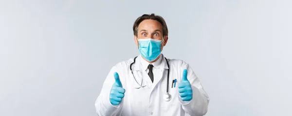 Covid-19 、ウイルス、医療従事者および予防接種の概念を防止する。親指を示す、医療用マスクや手袋で興奮し、驚きの幸せな医師は興奮し、素晴らしいニュースを聞いて、同意し、承認 — ストック写真