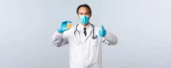 Covid-19, πρόληψη του ιού, εργαζόμενοι στον τομέα της υγείας και την έννοια του εμβολιασμού. Όλα καλά. Γιατρός με ιατρική μάσκα και γάντια εξετάζει δείγμα ούρων και δείχνουν τον αντίχειρα προς τα πάνω στην έγκριση, λευκό φόντο — Φωτογραφία Αρχείου