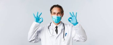 Covid-19, virüs, sağlık ve aşı konsepti. Doktor, klinikteki hizmetin kalitesini garanti eder ve garanti eder. Hastalar hastane çalışanlarına güvenebilir. Maskeli doktor ve eldivenler tamam işareti gösteriyor.