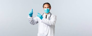 Covid-19, virüsü önleme, sağlık çalışanları ve aşı konsepti. Tıbbi maskeli ve eldivenli tatmin olmuş gülümseyen doktor test tüpünü aşı numunesiyle işaret ediyor, ilacı onaylıyor.