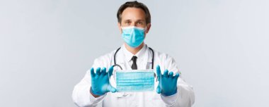 Covid-19, virüs, sağlık çalışanları ve aşı konsepti. PPE 'de orta yaşlı bir doktor, tıbbi maske markasını tavsiye ediyor, Coronavirus hastalığına yakalanmamak için maske takmasını açıklıyor.