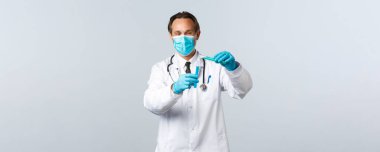 Covid-19, virüsü önleme, sağlık çalışanları ve aşı konsepti. Tıbbi maskeli ve eldivenli gülümseyen doktor başka bir test tüpüne kimyasal madde dökerek aşı testleri yapıyor.