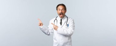 Covid-19, koronavirüs salgını, sağlık çalışanları ve pandemik konsept. Heyecanlı ve şaşırmış erkek doktor, çenenizi indirin ve kamerayı sol üst köşeye çevirin