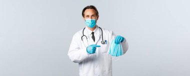 Covid-19, virüsü önleme, sağlık çalışanları ve aşı konsepti. PPE 'deki faydalı erkek doktor tıbbi maskeleri işaret ederek, koronavirüsün yakalanmasını önlemek için önlemler alınmasını öneriyor