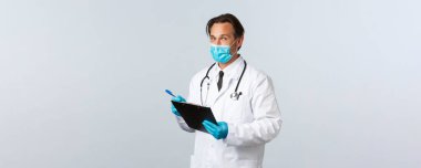 Covid-19, virüsü önleme, sağlık çalışanları ve aşı konsepti. Tıbbi maske ve eldiven giyen profesyonel bir doktor, elinde dosya, hasta semptomlarını yazıyor, klinikte koronavirüsle savaşıyor.