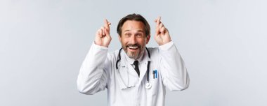 Covid-19, virüsü önleme, sağlık çalışanları ve aşı konsepti. İyimser, umut dolu, beyaz önlüklü, şans dileyen, gülümseyen, inançlı, dilek tutan doktorların yakın çekimi.