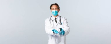 Covid-19, virüsü önleme, sağlık çalışanları ve aşı konsepti. Tıbbi maskeli ve eldivenli doktor, Coronavirus salgını sırasında el dezenfektanı kullanarak hijyenin önemini açıklıyor.