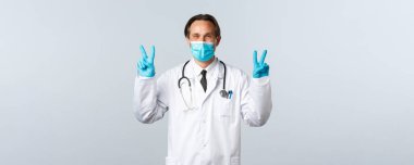 Covid-19, virüsü önleme, sağlık çalışanları ve aşı konsepti. Hevesli, tıbbi maskeli, eldivenli, barış belirtileri gösteren, V-işareti olan, iyimser bir doktor.