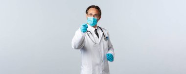 Covid-19, virüsü önleme, sağlık çalışanları ve aşı konsepti. Tıbbi maskeli ve eldivenli ciddi bir erkek doktor sosyal mesafeyi takip etmiyor.