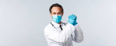 Covid-19, virüsü önleme, sağlık çalışanları ve aşı konsepti. Cesaretlendirilmiş ve kararlı iyimser doktor, tıbbi maske ve eldivenlerle, zafer için ellerinizi kenetleyin.