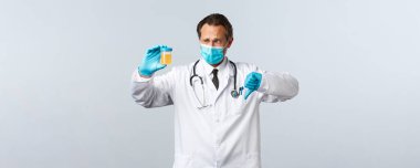 Covid-19, virüsü önleme, sağlık çalışanları ve aşı konsepti. Tıbbi maske ve eldiven giymiş hayal kırıklığına uğramış bir doktor idrar örneği gösteriyor, baş parmağının düşmesi kötü bir test sonucu, beyaz bir geçmiş.
