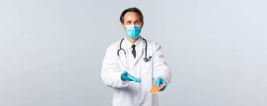 Covid-19, virüsü önleme, sağlık çalışanları ve aşı konsepti. Tıbbi maskeli ve eldivenli dost canlısı doktor tedaviyi işaret ediyor. Gripten alınan bu hapları kullanmanızı tavsiye ediyor.