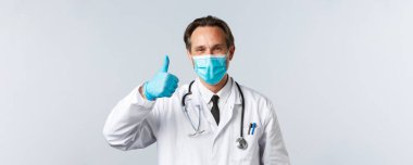 Covid-19, virüsü önleme, sağlık çalışanları ve aşı konsepti. Tıbbi maskeli ve eldivenli dost canlısı yakışıklı doktor onay verdi, ilaç ya da klinik hizmeti önerdi