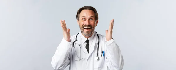 Covid-19, πρόληψη του ιού, εργαζόμενοι στον τομέα της υγείας και την έννοια του εμβολιασμού. Κοντινό πλάνο του ενθουσιασμένοι γενειοφόρος αρσενικό γιατρό σε λευκό παλτό σηκώνοντας τα χέρια μέχρι ενθουσιασμένος, ακούσει μεγάλη είδηση και χαρά — Φωτογραφία Αρχείου