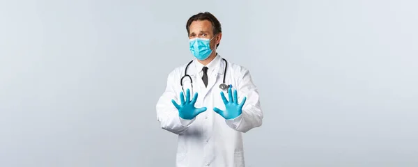 Covid-19, Prävention von Viren, Gesundheitspersonal und Impfkonzept. Widerwilliger oder angeekelter männlicher Arzt in medizinischer Maske und Handschuhen, Geste der Verweigerung zeigen, verleugnetes Händeschütteln, weißer Hintergrund — Stockfoto