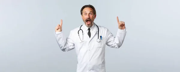 Covid-19, ξέσπασμα του ιού της στέψης, επαγγελματίες υγείας και πανδημία. Ενθουσιασμένος γιατρός σε λευκό παλτό και στηθοσκόπιο, δείχνοντας τα δάχτυλα ψηλά και λαχανιάζοντας κατάπληκτος, λέγοντας μεγάλα νέα — Φωτογραφία Αρχείου