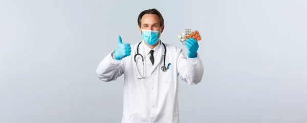 Covid-19, prevención de virus, trabajadores sanitarios y concepto de vacunación. Médico guapo satisfecho sonriendo, use máscara médica y guantes, pulgar hacia arriba como recomiendan pastillas, mostrar buena medicación —  Fotos de Stock