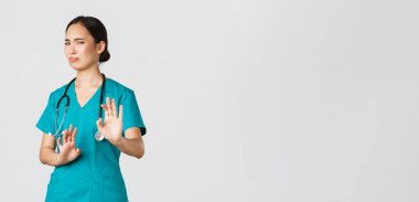 Covid-19, sağlık çalışanları, salgın konsepti. İsteksiz komik Asyalı hemşire, doktor birinden kaçıyor, geri çekil ve jesti durdur, suratını ekşitme, korkunç teklifi reddetme, reddetme, reddetme.