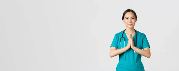 Covid-19, healthcare workers and preventing virus concept. Smiling kind and caring, pretty asian physician, female doctor in scrubs, showing namaste, praying gesture, white background — Stock Photo, Image