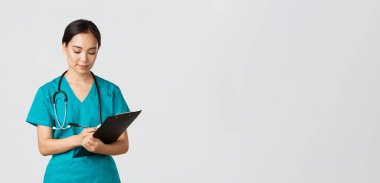 Sağlık çalışanları, virüsü önleme, karantina kampanyası konsepti. Ciddi görünümlü kadın doktor, önlüklü hemşire. Dosyaya bilgi yazıyor, hastayı muayene ediyor, beyaz bir geçmişi var.