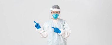 Covid-19, koronavirüs hastalığı, sağlık çalışanları konsepti. Küstah profesyonel Asyalı doktor, doktor ya da teknisyen üst sol köşeyi işaret eden kişisel koruyucu ekipman.
