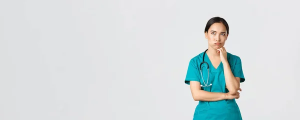 Covid-19, healthcare workers, pandemic concept. Annoyed and bothered asian female doctor, nurse on her shift looking irritated or tired, eye roll bored and exhale, standing white background in scrubs — Stock Photo, Image