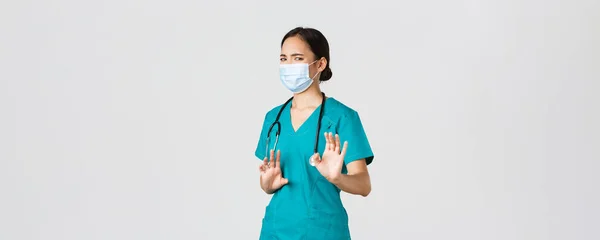 Covid-19, coronavirus ziekte, gezondheidswerkers concept. Ontevreden Aziatische vrouwelijke arts, arts of verpleegkundige vermijden contact met ziektekiemen, dragen medische masker en scrubs, schudden handen weigeren — Stockfoto