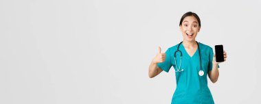 Covid-19, sağlık çalışanları ve online tıp konsepti. Koronavirüs sırasında yeni bir mesafe danışma yöntemi deneyen Asyalı kadın doktor akıllı telefon uygulaması ve onaylama gösteriyor.