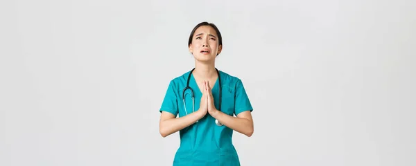 Covid-19, pracownicy służby zdrowia, koncepcja pandemii. przepracowany smutny i zmęczony Azji lekarz, pielęgniarka błagając o pomoc, błagając Boga i płacząc ze stresu, stojąc białe tło — Zdjęcie stockowe