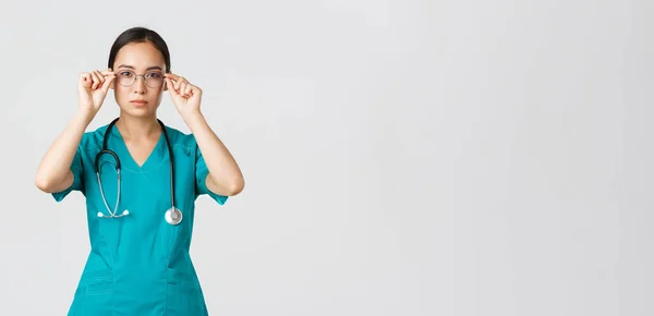 Covid-19, trabajadores de la salud, concepto pandémico. Confiado serio y determinado médico asiático, enfermera en matorrales se puso gafas, listo para el turno en la sala de emergencias, fondo blanco —  Fotos de Stock