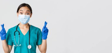 Covid-19, koronavirüs hastalığı, sağlık çalışanları konsepti. Heyecanlı ve umut dolu Asyalı doktor, sağlık maskeli hemşire ve lastik eldiven şans dileyin, dileğinizi gerçekleştirin, beyaz arka plan